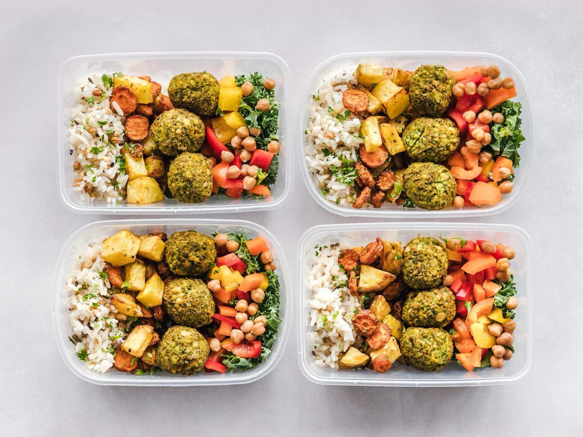 Quatre boîtes de conservation alignées, chacune garnie de riz, de boulettes de falafel, de pois chiches, de légumes rôtis et de crudités