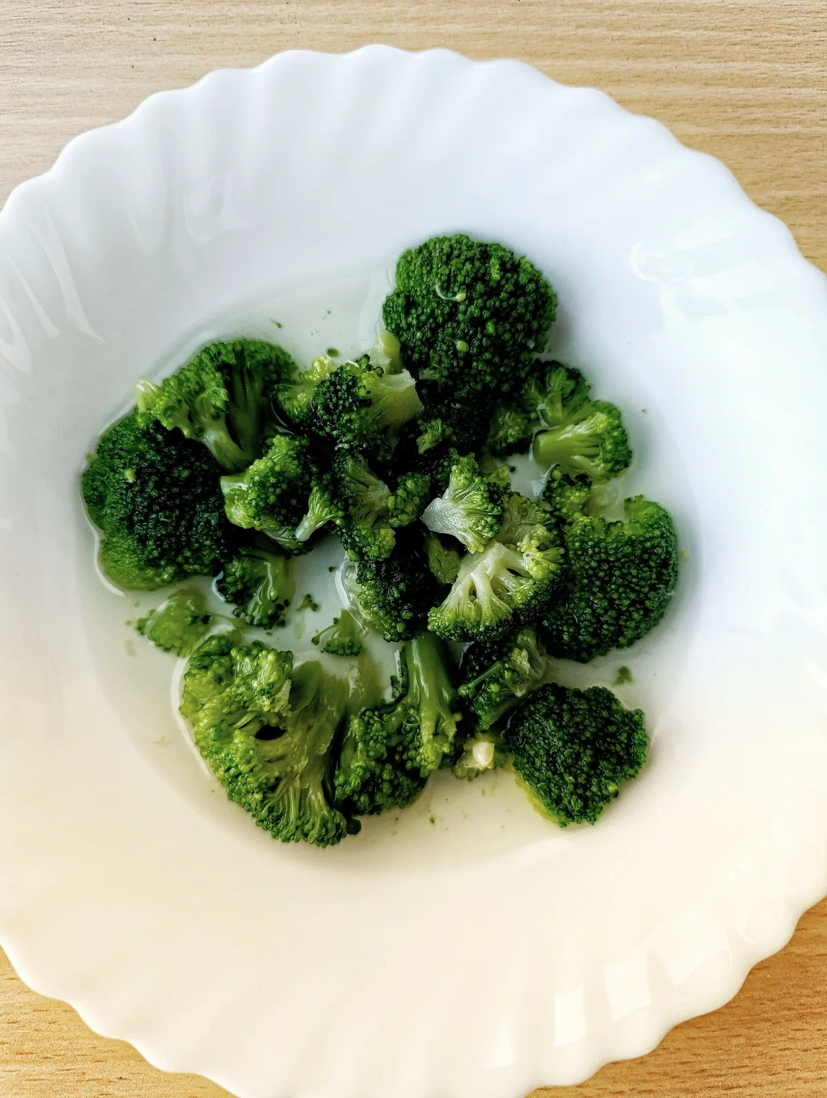 Des bouquets de brocoli cuits, vert vif, dans une assiette blanche à bord festonné