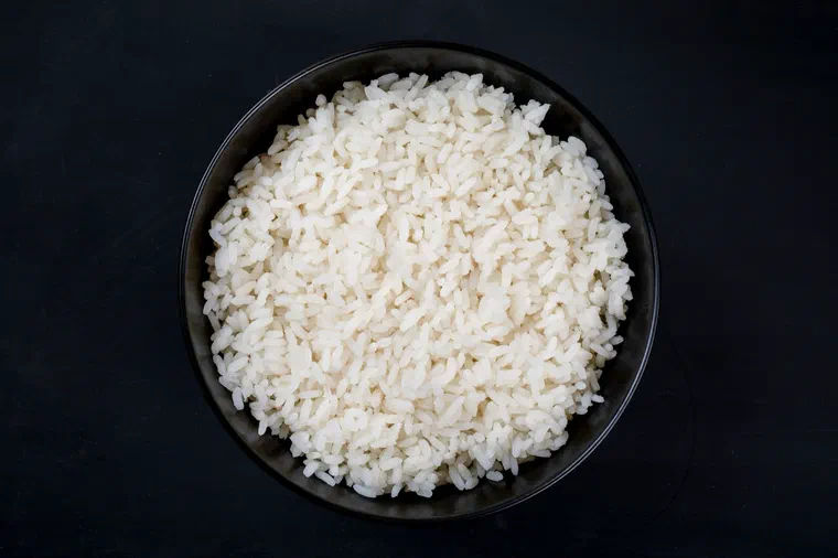 Un bol noir rempli de riz blanc cuit aux grains bien détachés, vu de dessus sur un fond sombre
