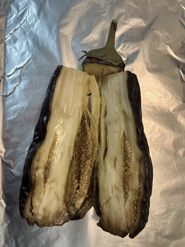 Une aubergine rôtie ouverte en deux dans la longueur, chair fondante et peau violette plissée, posée sur une feuille d'aluminium