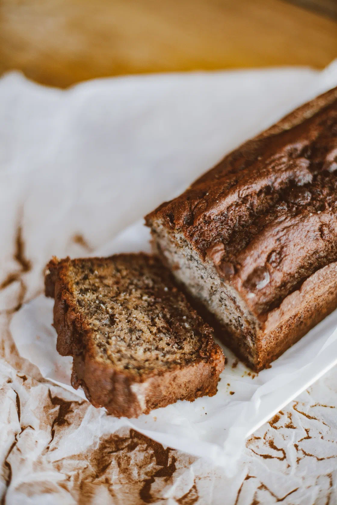 Un banana bread à la croûte brune et craquelée, entamé, avec une tranche coupée posée sur du papier sulfurisé