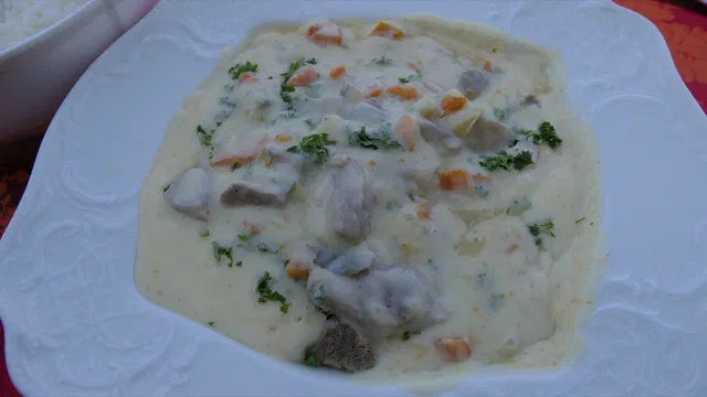 Blanquette de veau dans une assiette creuse blanche : morceaux de veau, dés de carotte et persil dans une sauce crémée, un bol de riz blanc à côté