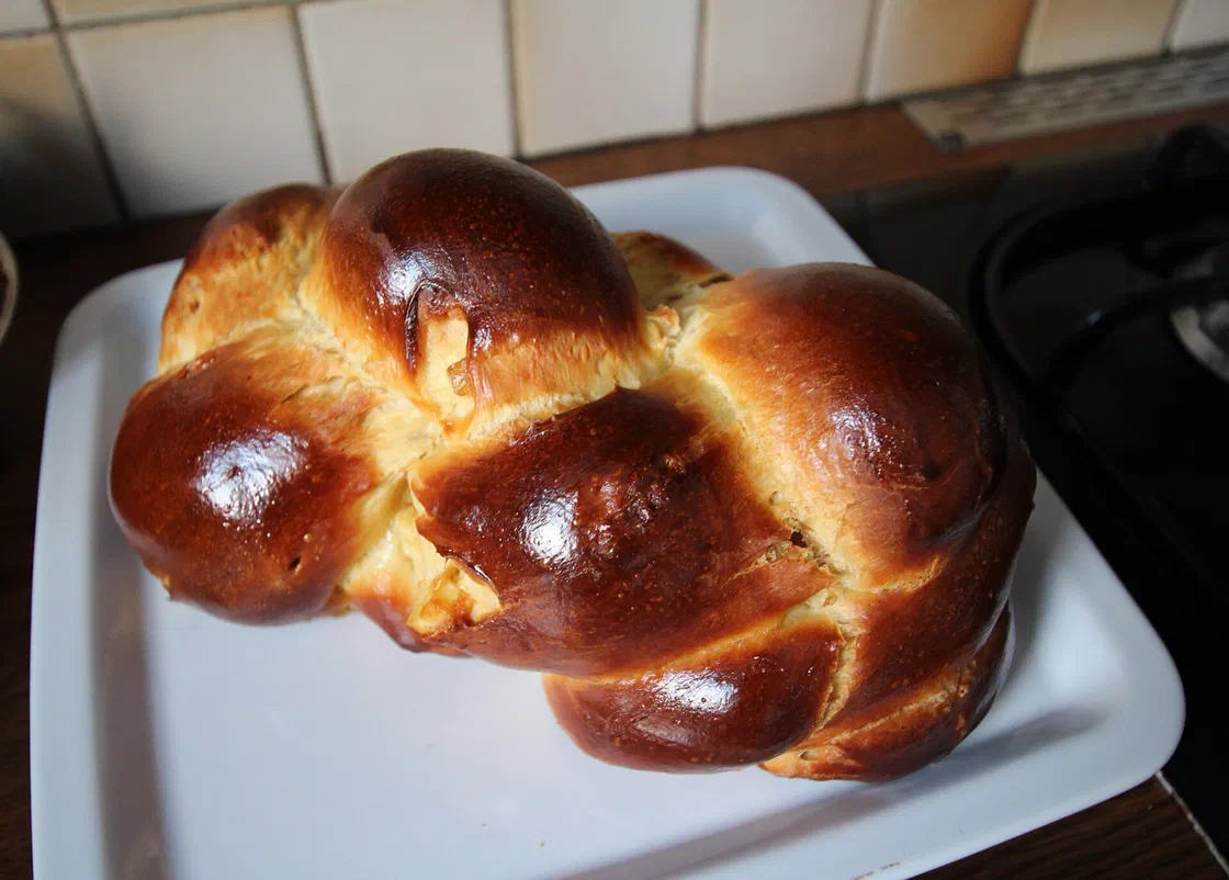 Une brioche tressée bien dorée et brillante posée sur un plat blanc