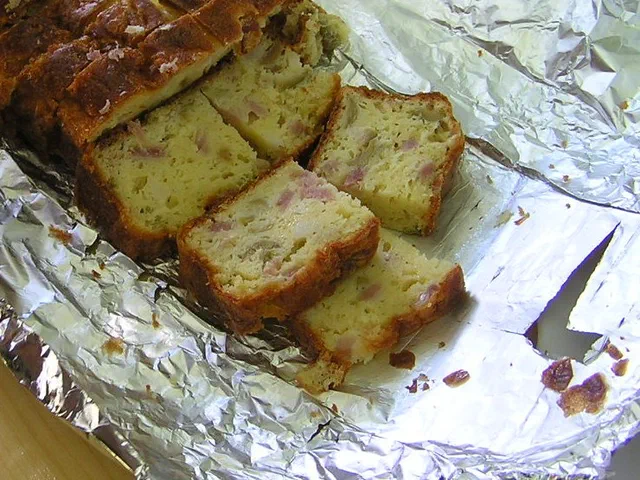 Un cake salé au jambon coupé en tranches épaisses sur une feuille d'aluminium, la mie jaune parsemée de dés de jambon
