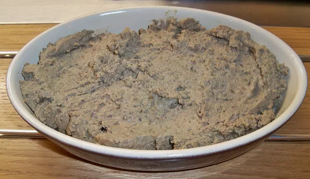 Caviar d'aubergine à la texture hachée, gris-brun, étalé dans un plat ovale en céramique blanche