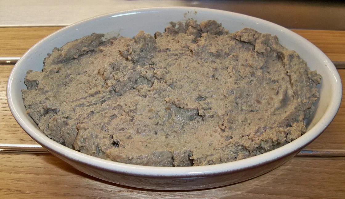 Caviar d'aubergine à la texture hachée, gris-brun, étalé dans un plat ovale en céramique blanche