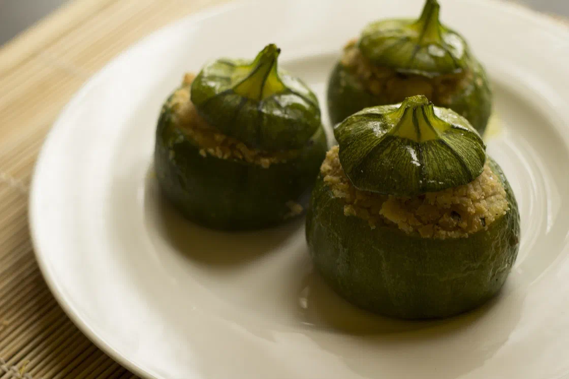Trois courgettes rondes farcies, leur chapeau posé sur la farce dorée, dans une assiette blanche