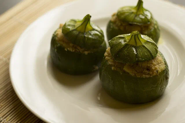 Trois courgettes rondes farcies, leur chapeau posé sur la farce dorée, dans une assiette blanche