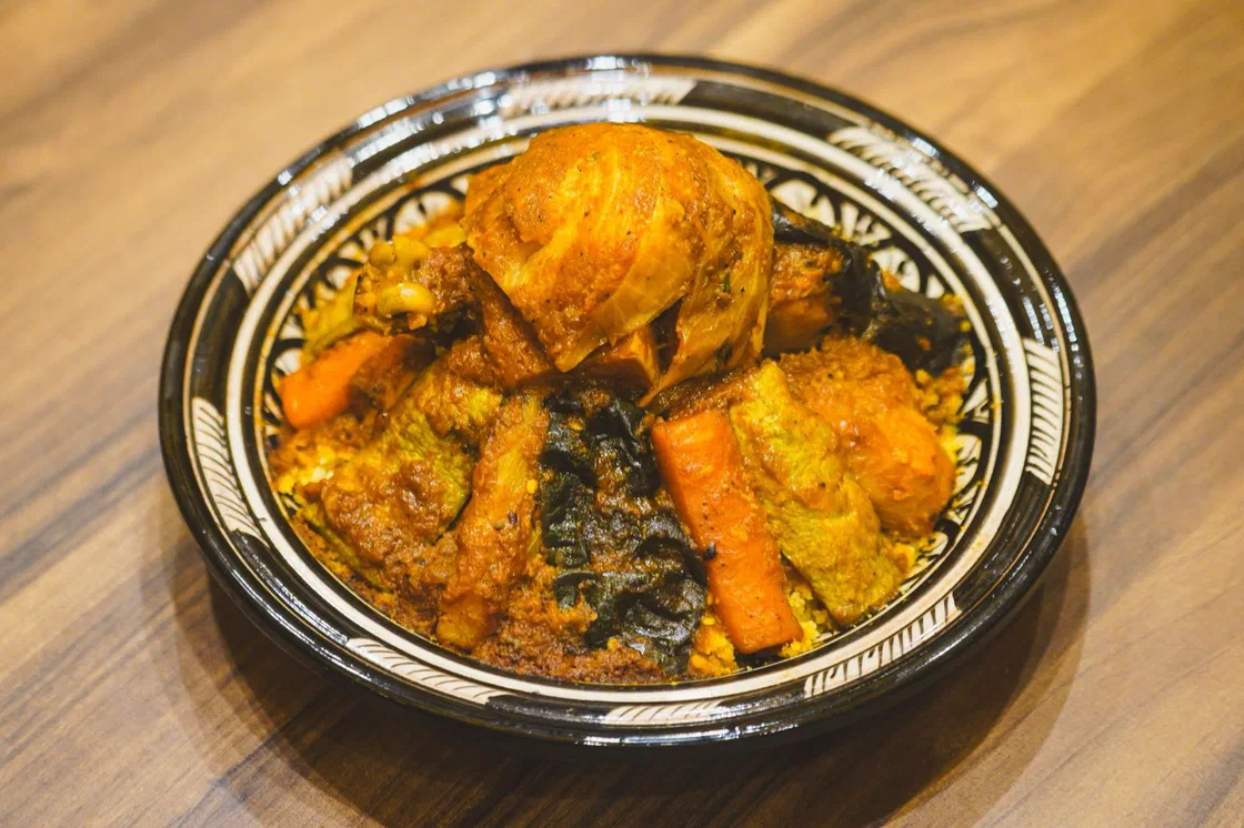Couscous au poulet dans un plat marocain peint : cuisse de poulet dorée posée sur la semoule, entourée de carottes, courgettes, courge et quelques pois chiches