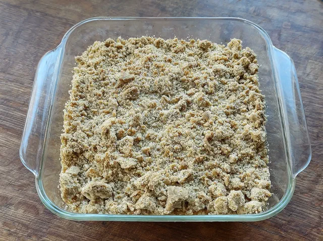 Un crumble aux pommes cuit dans un plat carré en verre, couvert d'une pâte sablée en grosses miettes