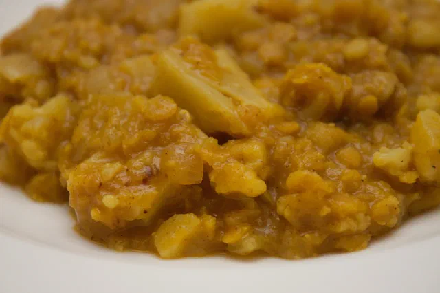 Gros plan sur un curry orangé de lentilles corail fondues et de morceaux de chou-fleur dans une assiette blanche