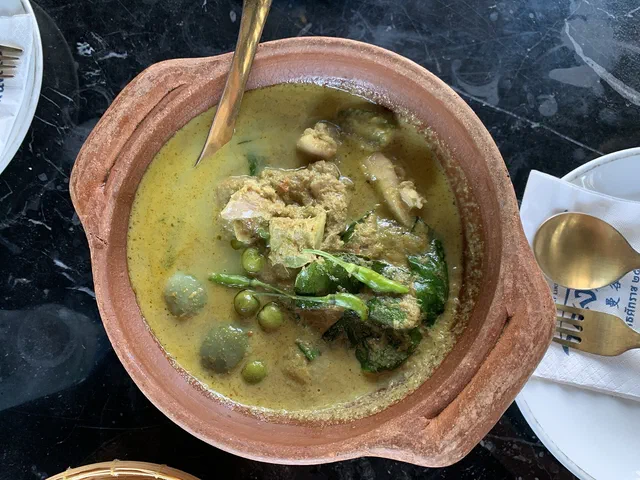 Un curry vert thaï dans un plat creux en terre cuite, avec des morceaux de viande, des aubergines thaïes rondes, des aubergines pois et des feuilles de basilic dans une sauce coco verdâtre