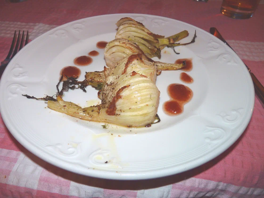 Des demi-bulbes de fenouil cuits jusqu'à être fondants et légèrement dorés, servis sur une assiette blanche avec quelques points de sauce