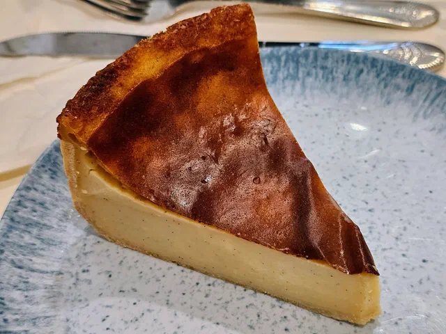 Une part de flan pâtissier au dessus brun caramélisé, crème jaune pâle sur fond de pâte, posée sur une assiette