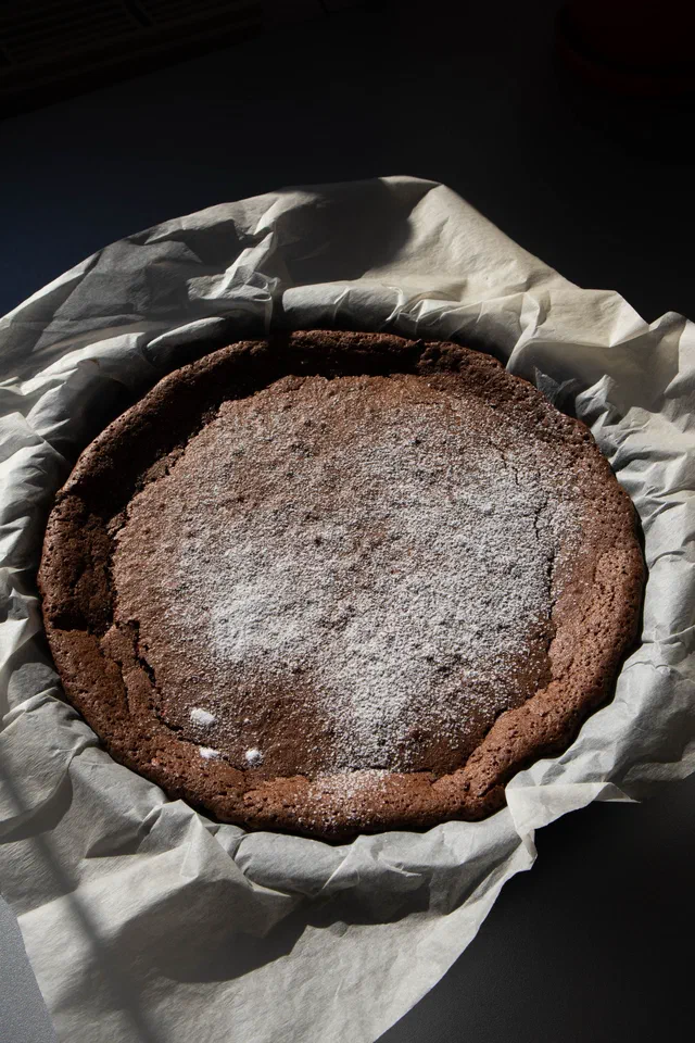 Un gâteau au chocolat rond tout juste sorti du four, saupoudré de sucre glace, encore dans son papier cuisson