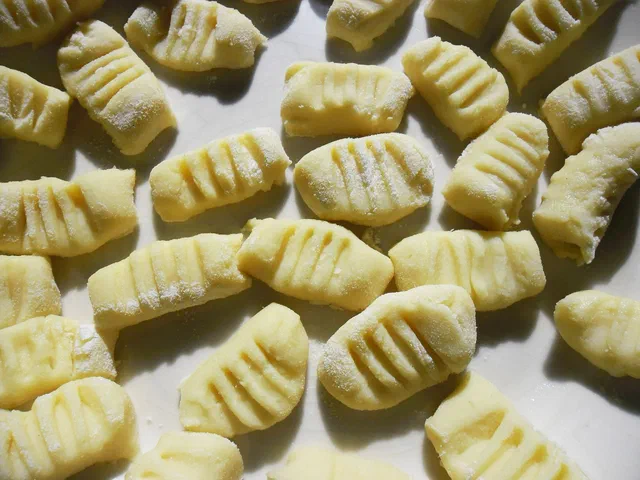 Des gnocchis de pommes de terre crus, striés à la fourchette, étalés sur un plan de travail fariné avant la cuisson