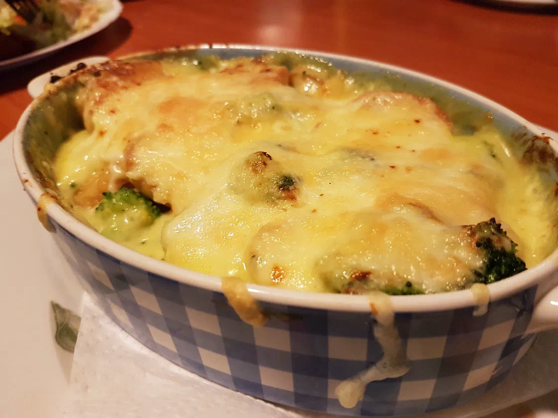 Un plat à gratin individuel avec des bouquets de brocoli et des pommes de terre sous une couche de fromage fondu et doré