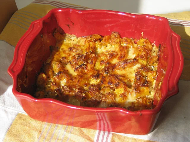 Un gratin de courge butternut doré et bien gratiné dans un plat rectangulaire rouge, posé sur un torchon