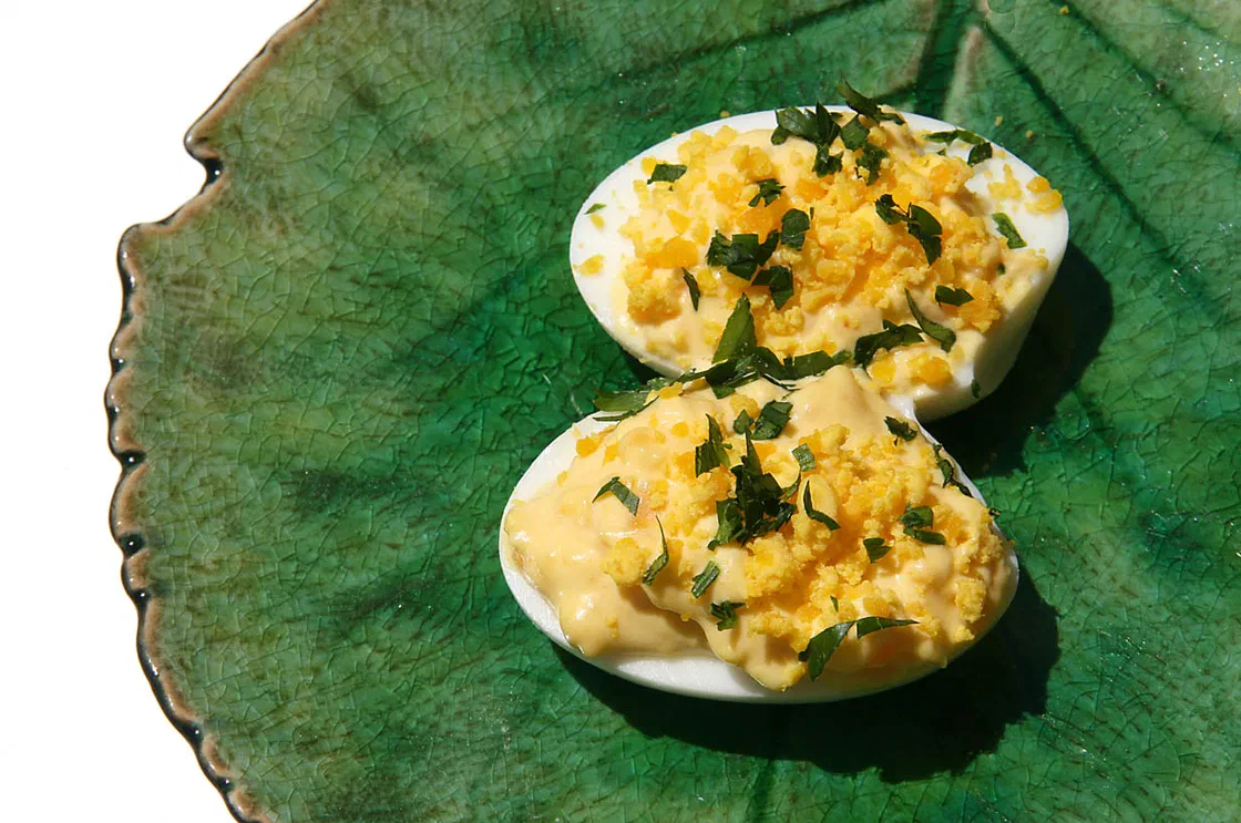 Deux demi-œufs durs garnis de farce jaune à la mayonnaise, de jaune émietté et de ciboulette, sur une assiette verte en forme de feuille