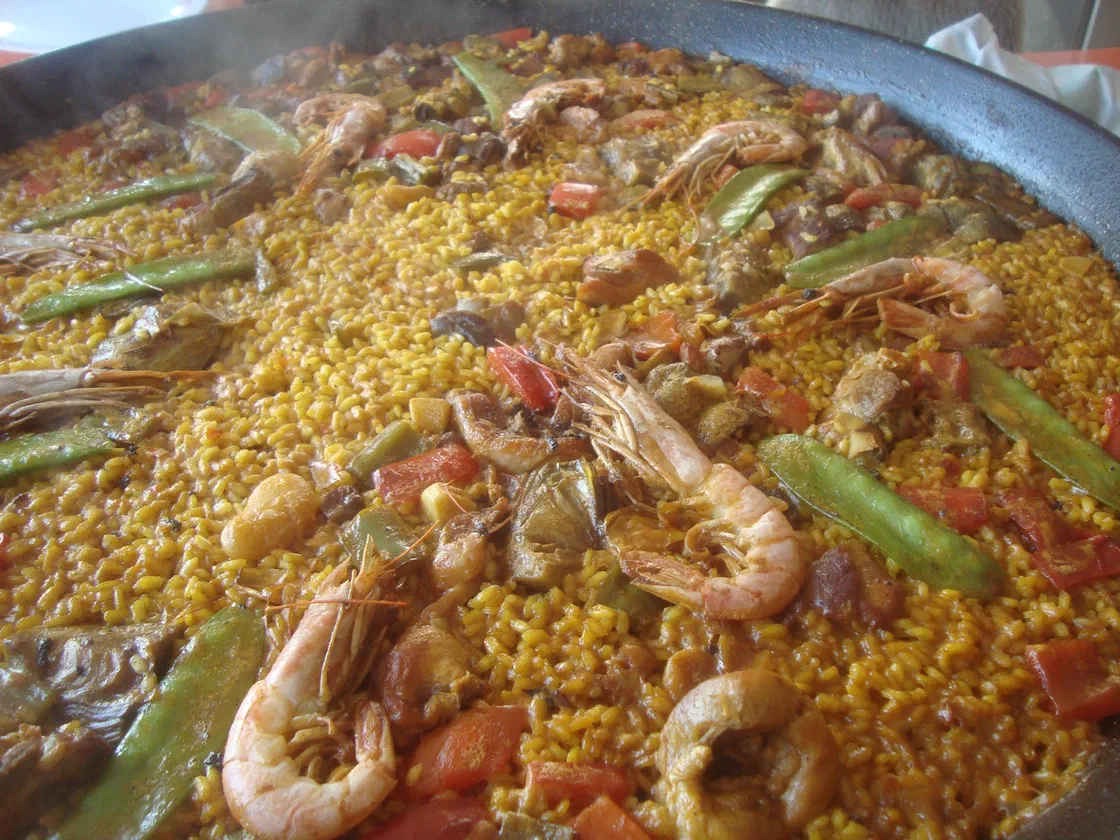 Une paella dans sa poêle, avec des crevettes entières, des pois gourmands et du riz jaune au safran