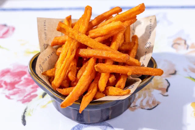 Frites de patate douce orangées et croustillantes dans un petit bol bleu garni de papier