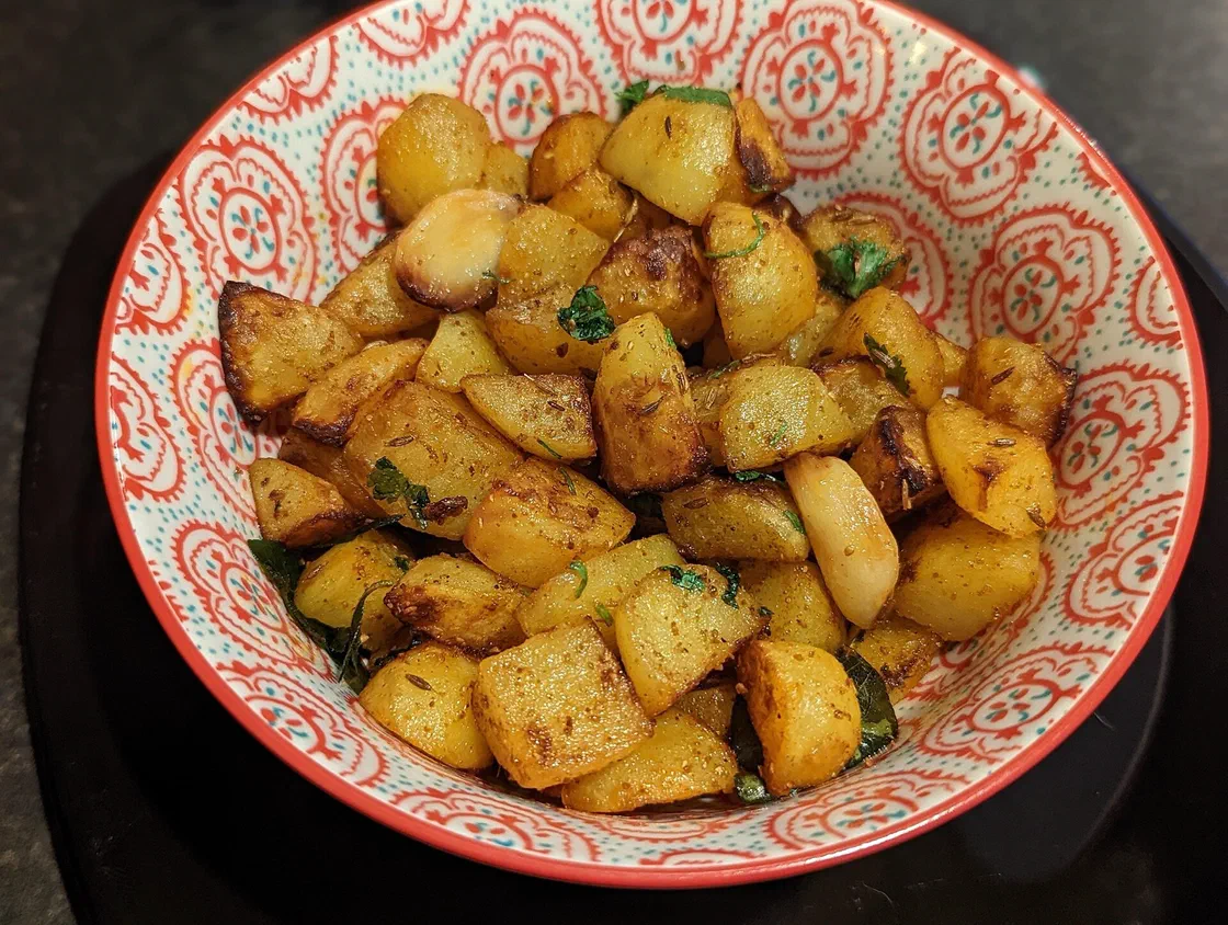 Cubes de pommes de terre rôtis et dorés, parsemés de graines de cumin et de coriandre fraîche, dans un bol à motifs rouges