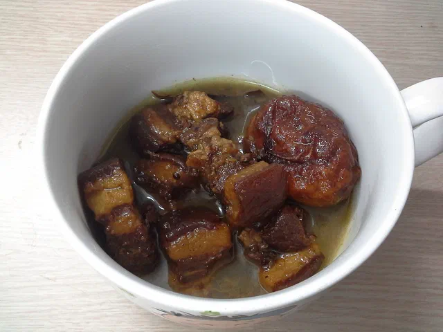 Cubes de poitrine de porc braisés au caramel dans un bol blanc, avec leur sauce ambrée et un œuf dur coloré par la cuisson