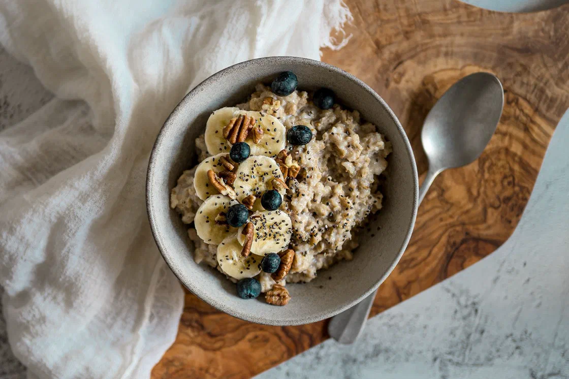 Un bol de porridge aux flocons d'avoine garni de rondelles de banane, de myrtilles, de noix de pécan et de graines de chia, avec une cuillère