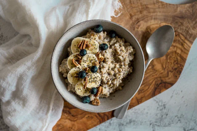 Un bol de porridge aux flocons d'avoine garni de rondelles de banane, de myrtilles, de noix de pécan et de graines de chia, avec une cuillère