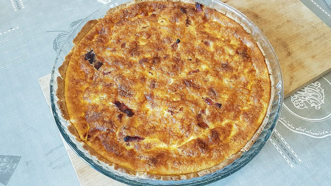 Quiche lorraine entière et dorée dans un moule en verre, posée sur une planche
