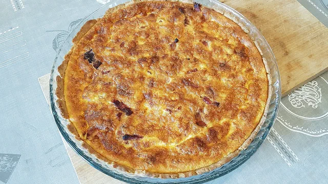 Quiche lorraine entière et dorée dans un moule en verre, posée sur une planche