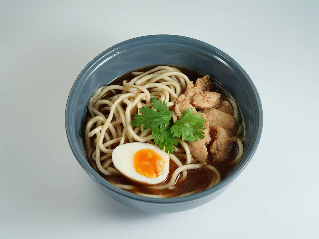 Un bol de ramen au bouillon brun avec des nouilles, des morceaux de poulet, un demi-œuf mollet et de la coriandre