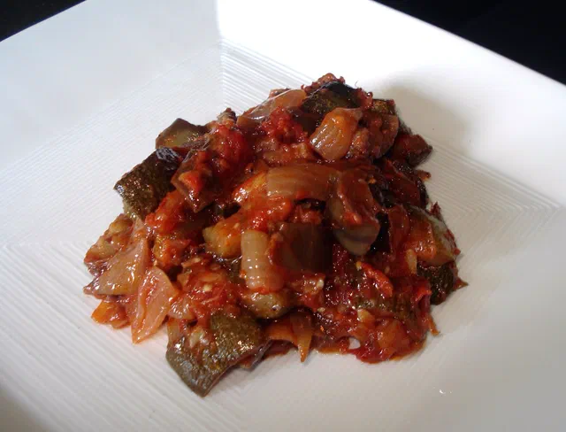 Une portion de ratatouille aux morceaux d'aubergine, de poivron et de tomate, servie sur une assiette blanche