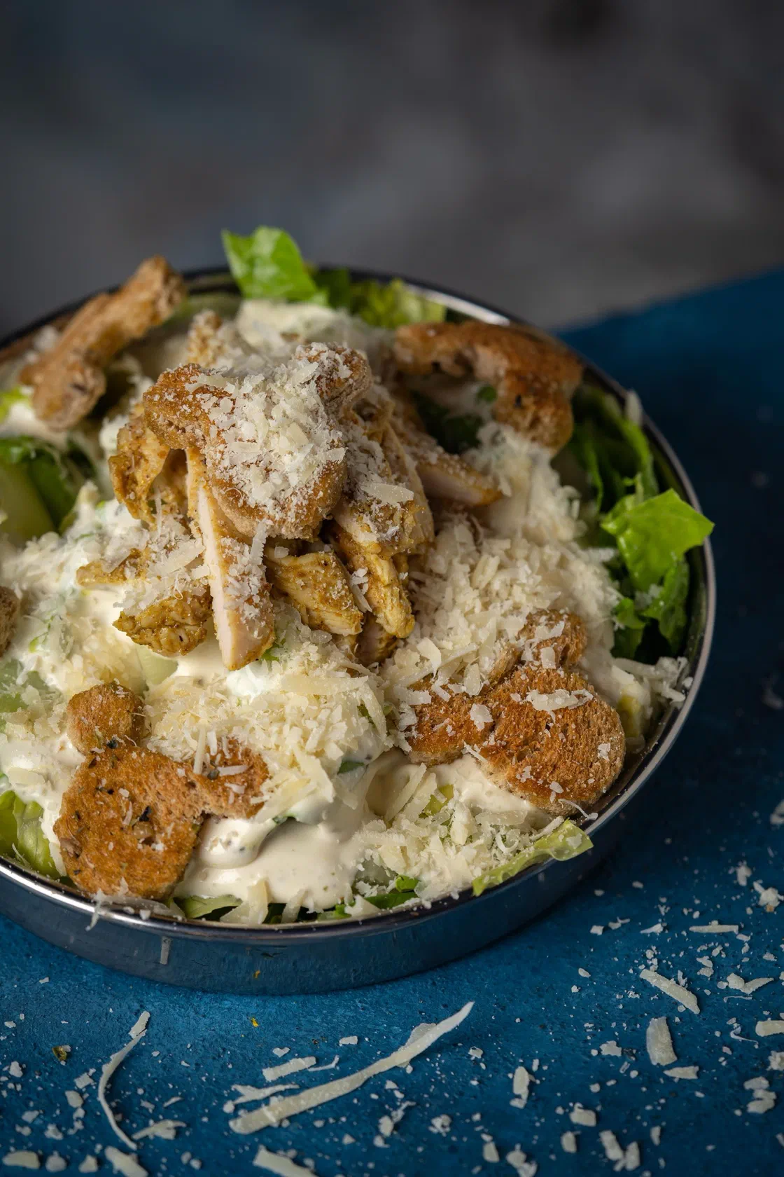 Une salade César dans un bol, avec des morceaux de poulet grillé, des croûtons et beaucoup de parmesan râpé