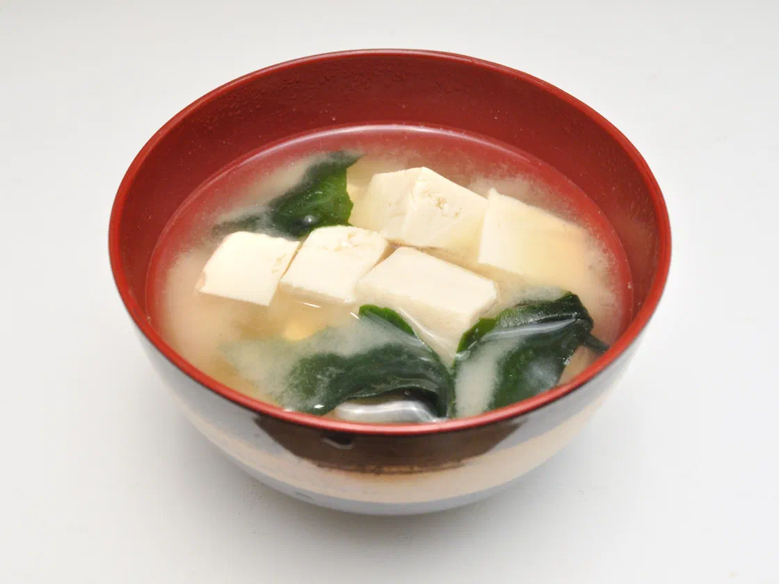 Un bol laqué rouge de soupe miso avec des cubes de tofu blanc et des feuilles de wakame