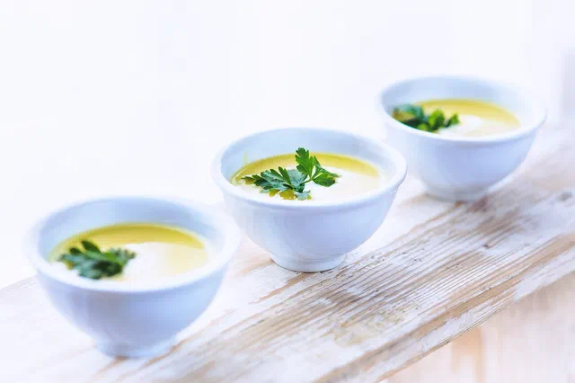 Trois petits bols blancs de soupe poireaux pommes de terre mixée, couleur crème, décorés d'une feuille de persil, sur une planche en bois blanchi